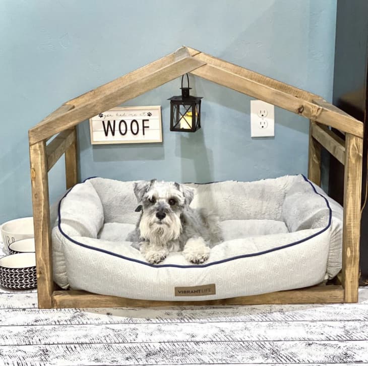 house-shaped wood frame surrounding cushioned dog bed