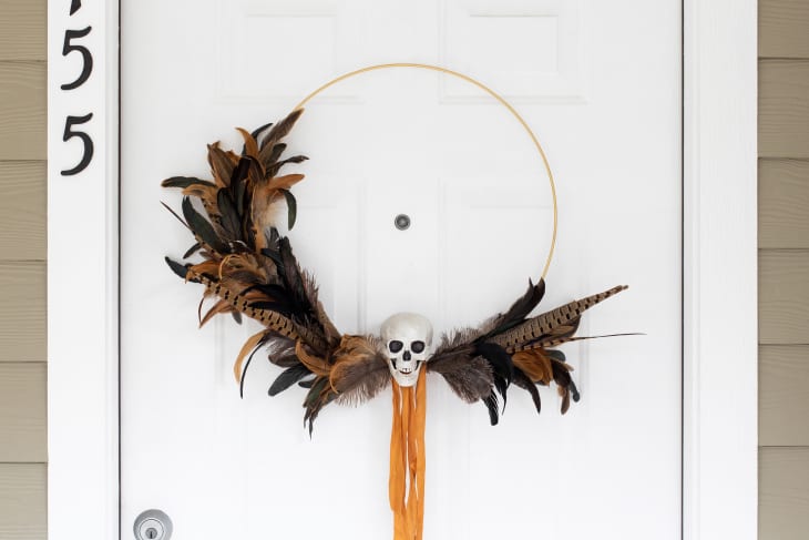 Halloween wreath on front door made with feathers and a gold hoop, with a skull accent