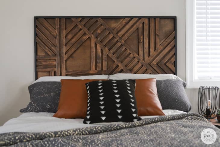 Dark wooden geometric headboard behind bed with gray linens