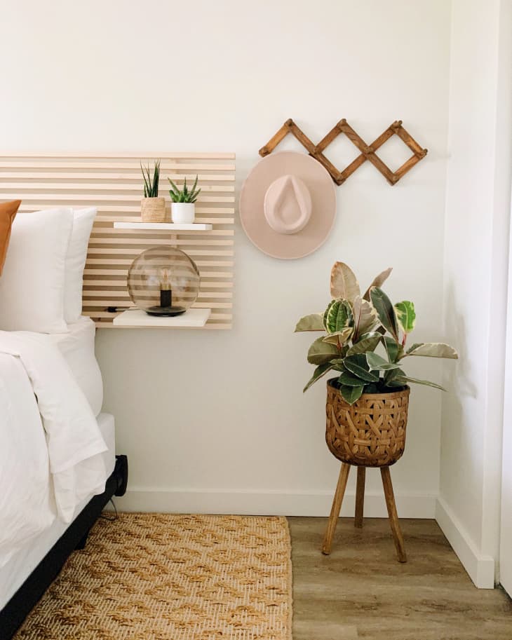 Bedroom with DIY wood slat headboard, coat hooks, and plant in corner