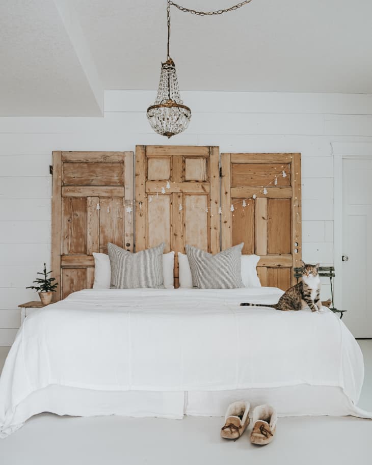 Bed with white linens and neutral headboard made of reclaimed doors