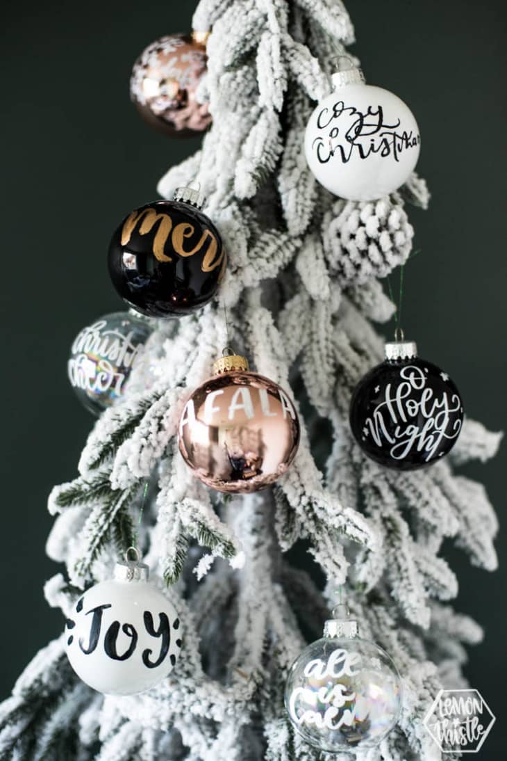 Black, gold, and white ornaments with hand lettering hanging on snowy tree