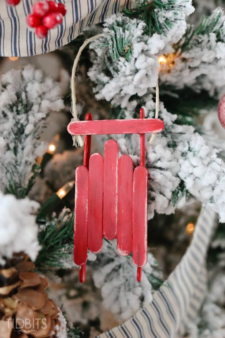 Red sled ornament made of popsicle sticks hanging on tree
