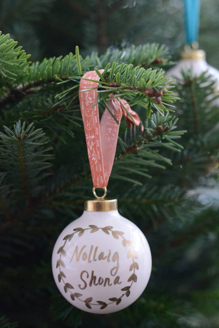Gold writing on white ball ornament hanging from tree