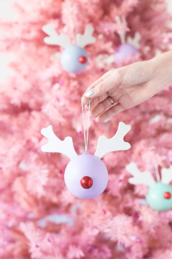 Hand holding Rudolph ornament against pink background