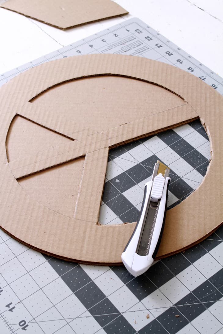 using a craft knife to cut a peace symbol out of cardboard round