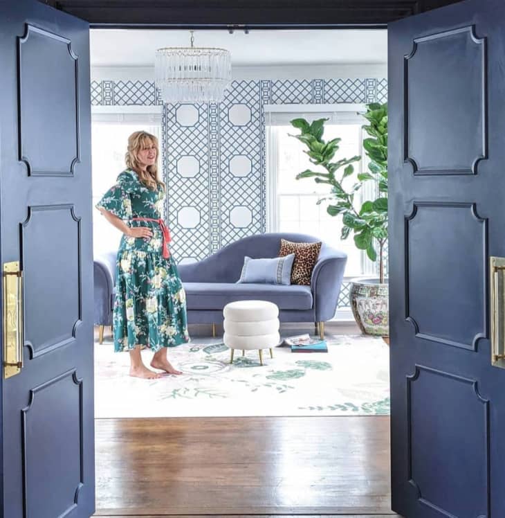View of woman standing in living room through doorway with two blue doors with moulding