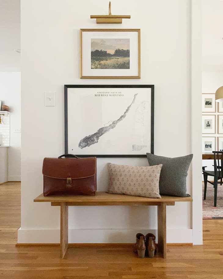 entryway with small bench under two framed pieces of art and a sconce
