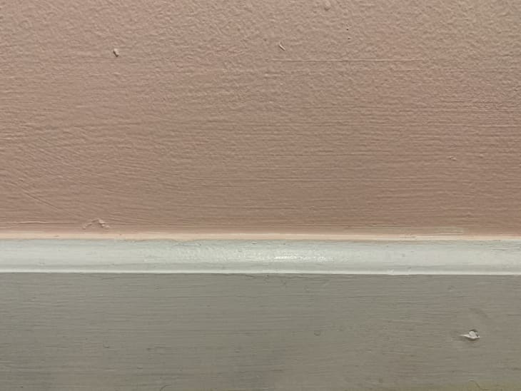 close-up view of wall painted with coral paint, which has dripped onto white baseboards