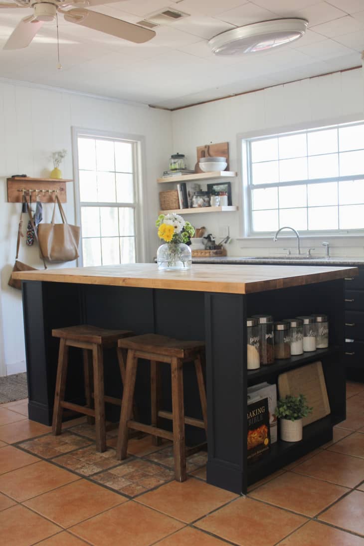 gray kitchen island with wood top and open shelves on one end.