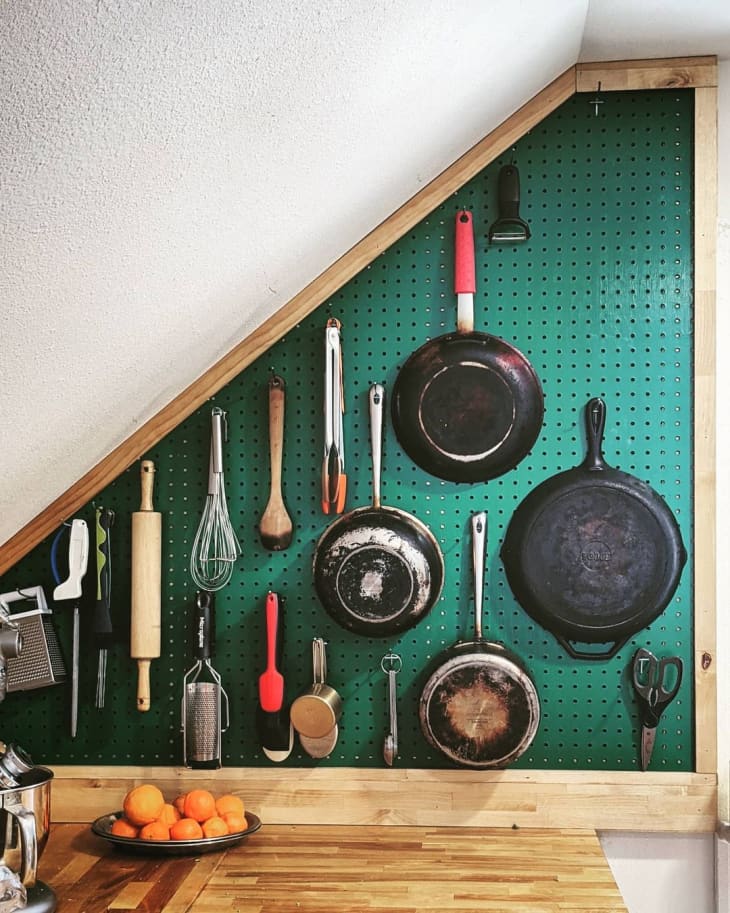 green pegboard on a small wall filled with pans and cooking utensils