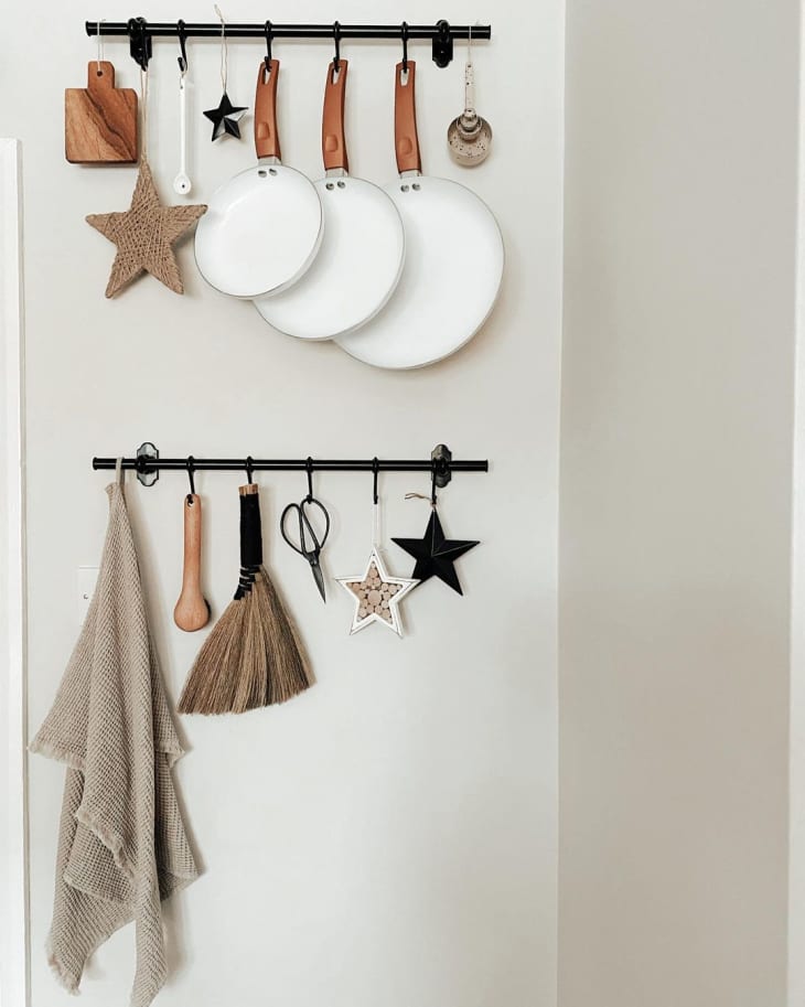 two railings installed on an empty wall, with pans, kitchen tools, and accessories hanging from them via S-hooks