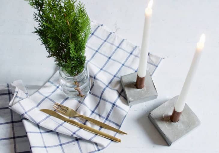 Candlesticks with concrete base next to blue-checked napkin and plant