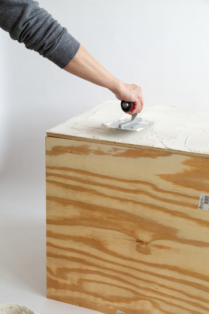 Hand adding adhesive to wooden box with trowel