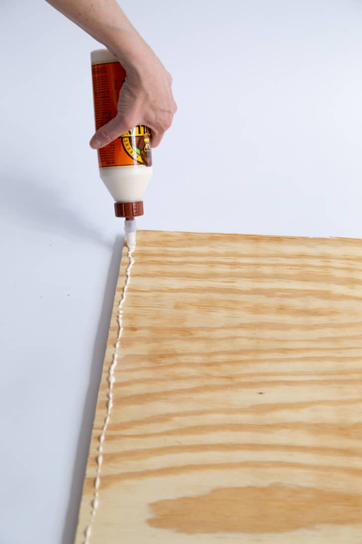 Hand applying wood glue to sheet of wood