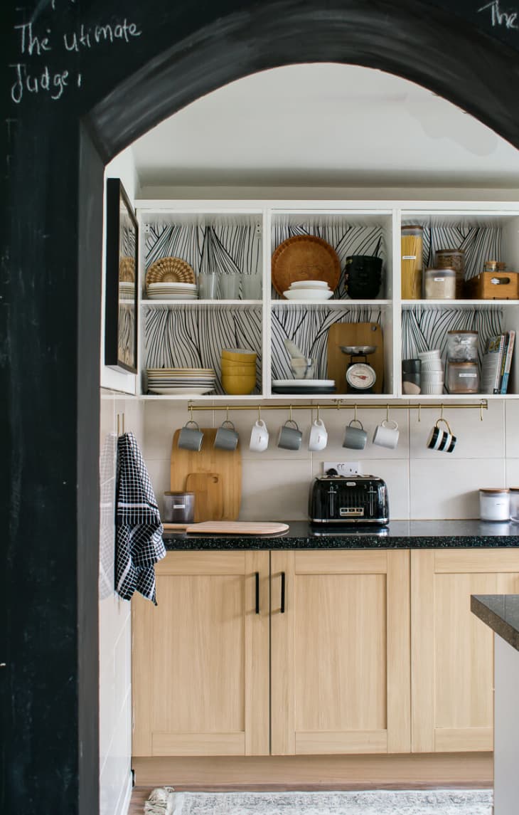 kitchen with wood lower cabinets, open uppers, and black and white wallpaper backing