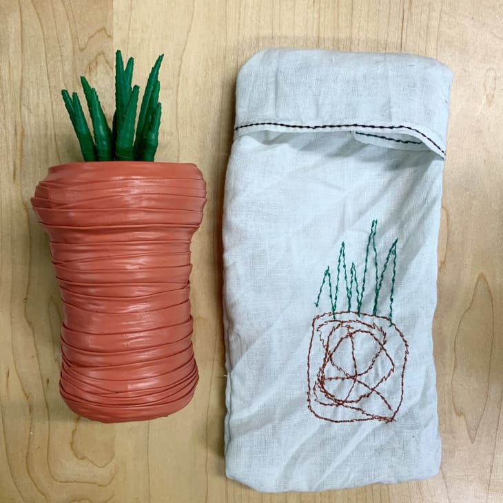faux potted plant made from paint, next to a small fabric carrying bag with an embroidered sketch of the faux plant