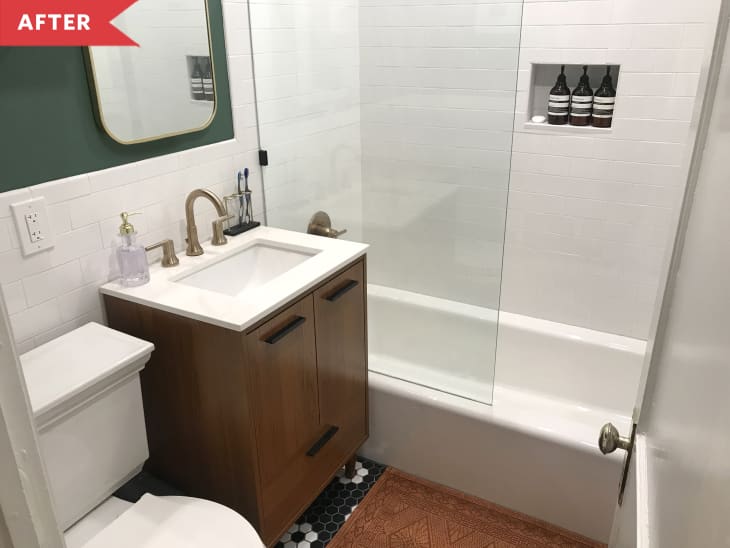 After: Bathroom with green walls, white tile, brown wooden vanity, black and white penny tiles, and rust-colored bath mat
