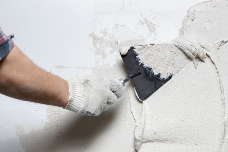 hand applying wet plaster to a wall with a trowel