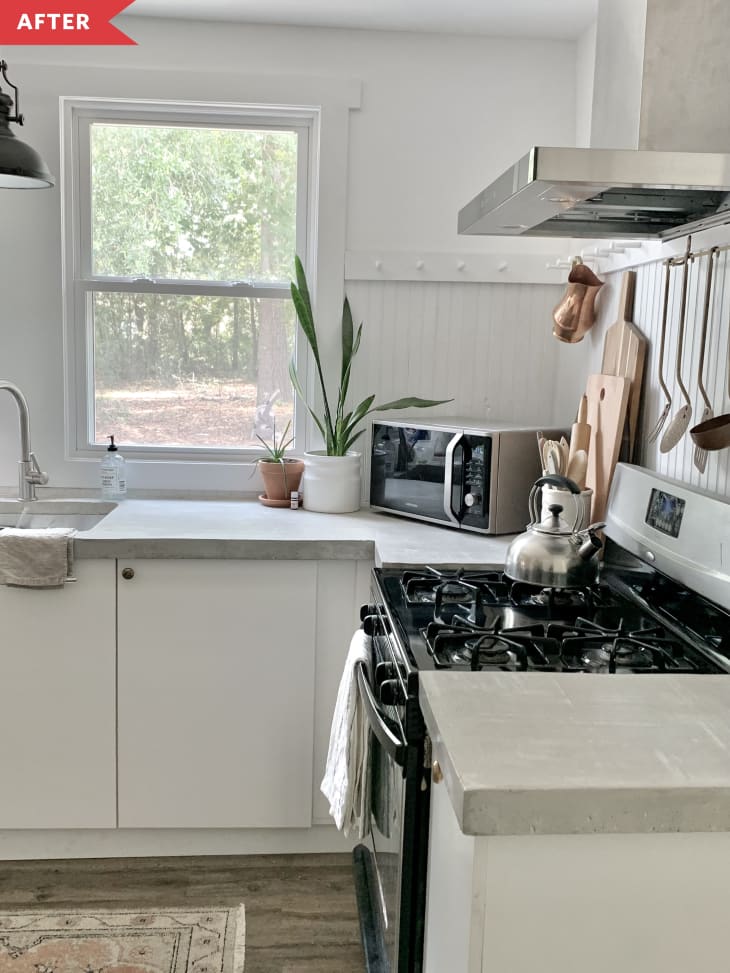 After: White kitchen with gray concrete counters, open shelving, and black and stainless steel appliances