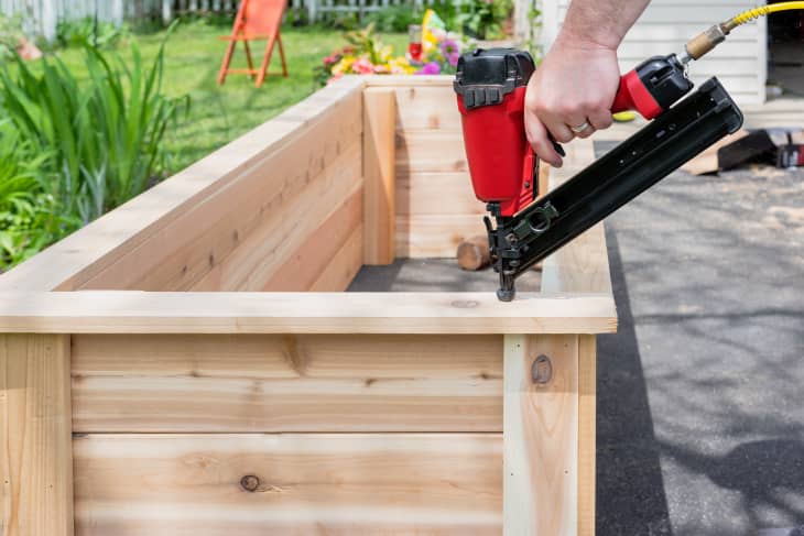 hand using a pneumatic nailer to add trim to the top of a cedar planter