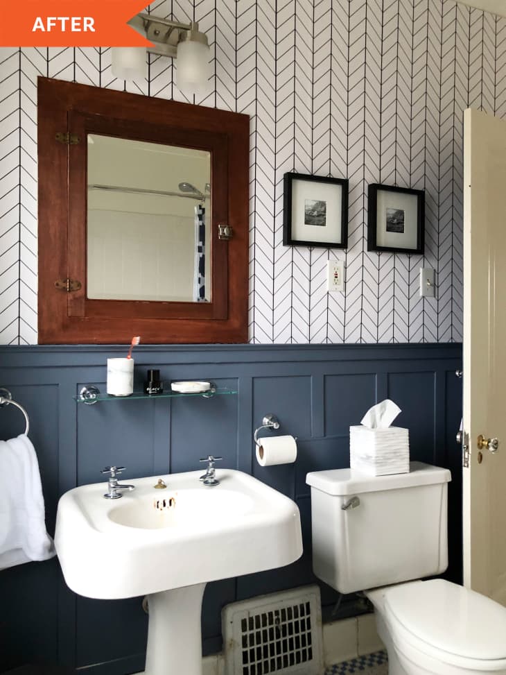 After: wooden framed mirror hangs over bathroom sink on a wall with a white and black pattern on top and blue/gray wooden paneling beneath