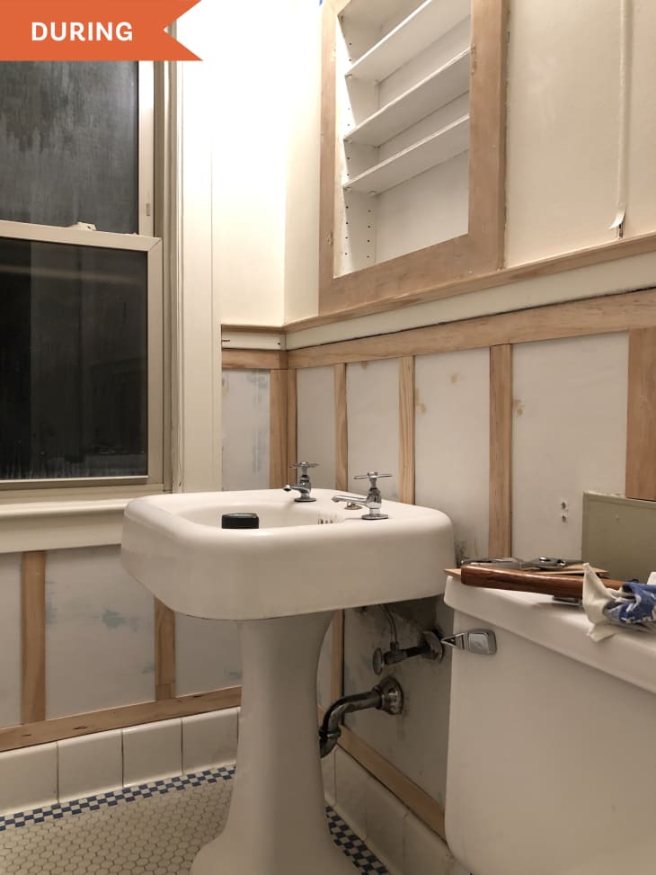 During: Walls of bathroom with wooden trim added and shelving above vanity