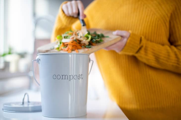 person putting food scraps into a countertop compost container