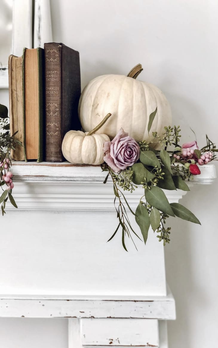 A white mantel with white pumpkins and books on top