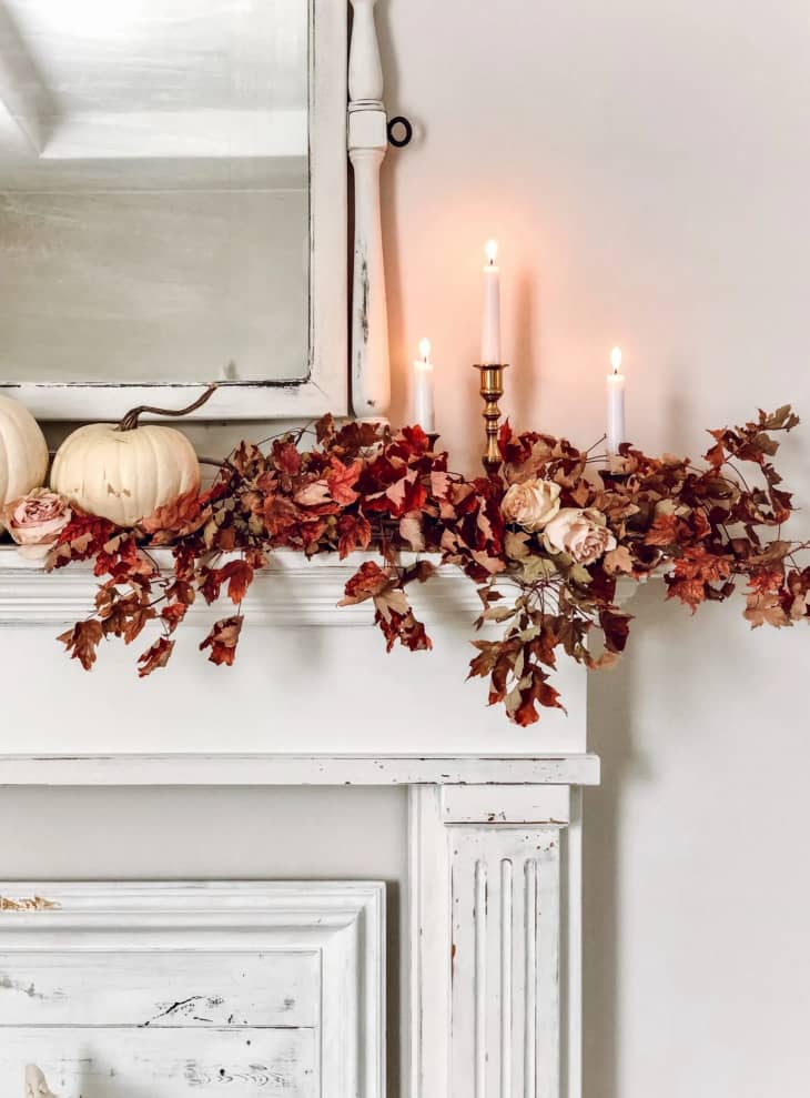 A white mantel with red garland and candles on top
