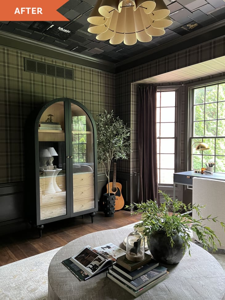 After: Office with plaid wallpapered walls, and black textured ceiling with a pleated pendant light. A desk sits in front of a bay window. There is a glass-doored arched cabinet on the wall.