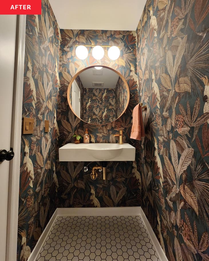 After: a round bathroom mirror above a sink surrounded by tropical wallpaper
