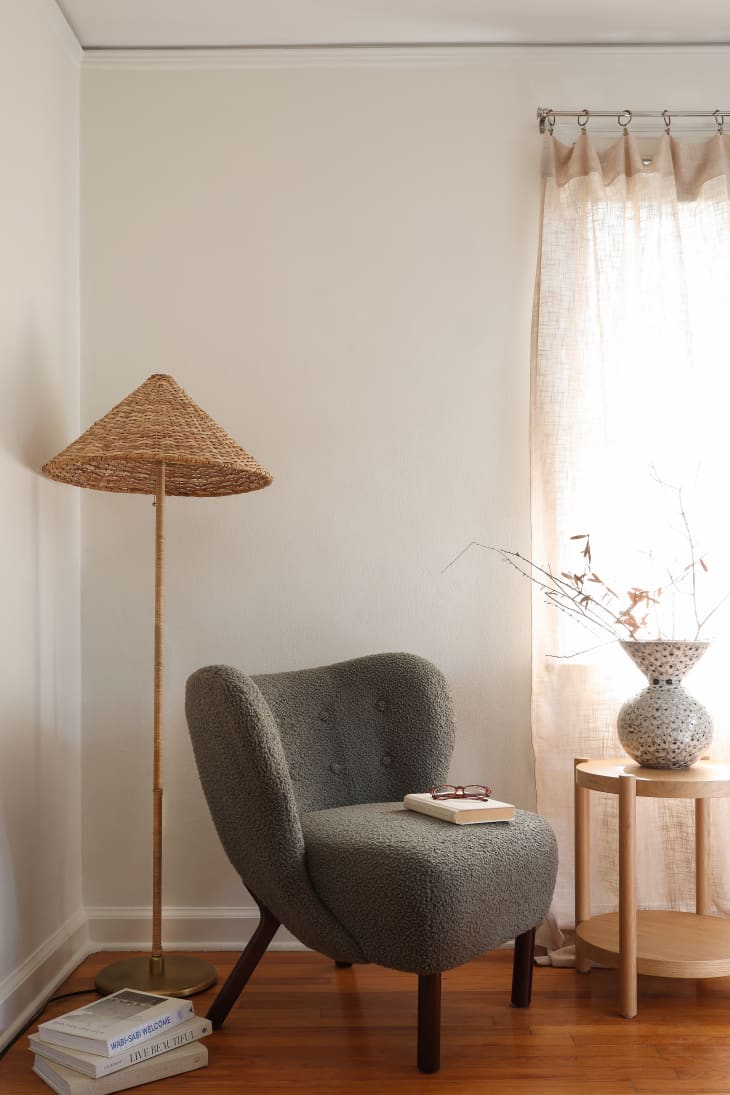 A room with white walls, a green chair, and a floor lamp with a wicker shade.