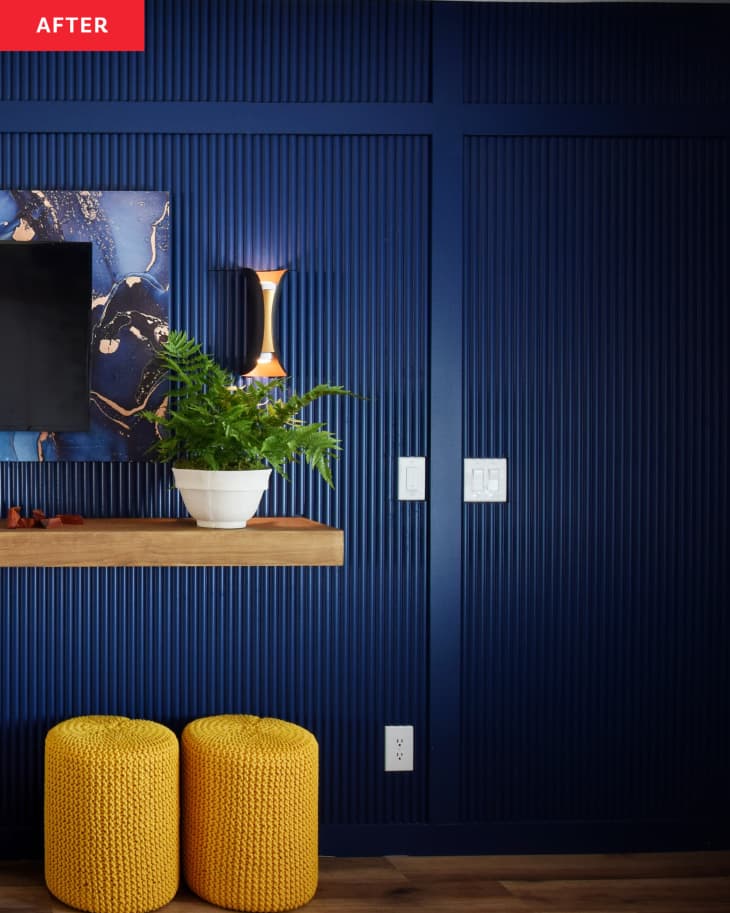 After: a dark blue wall with a tv mounted above a wooden shelf and two yellow ottomans on the floor