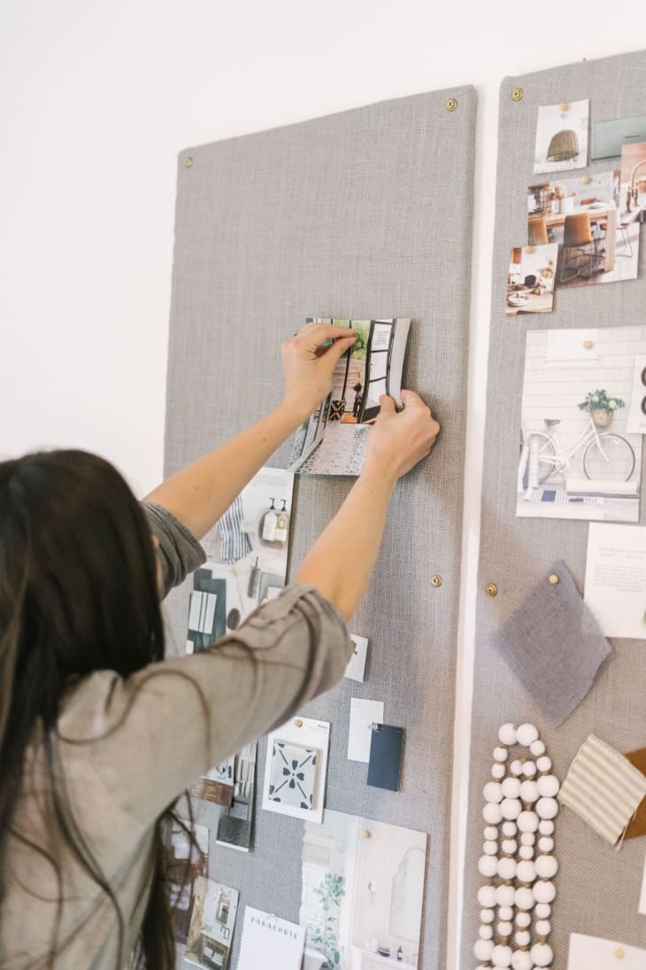 woman pinning a photo to a DIY bulletin board covered in a grayish burlap fabric
