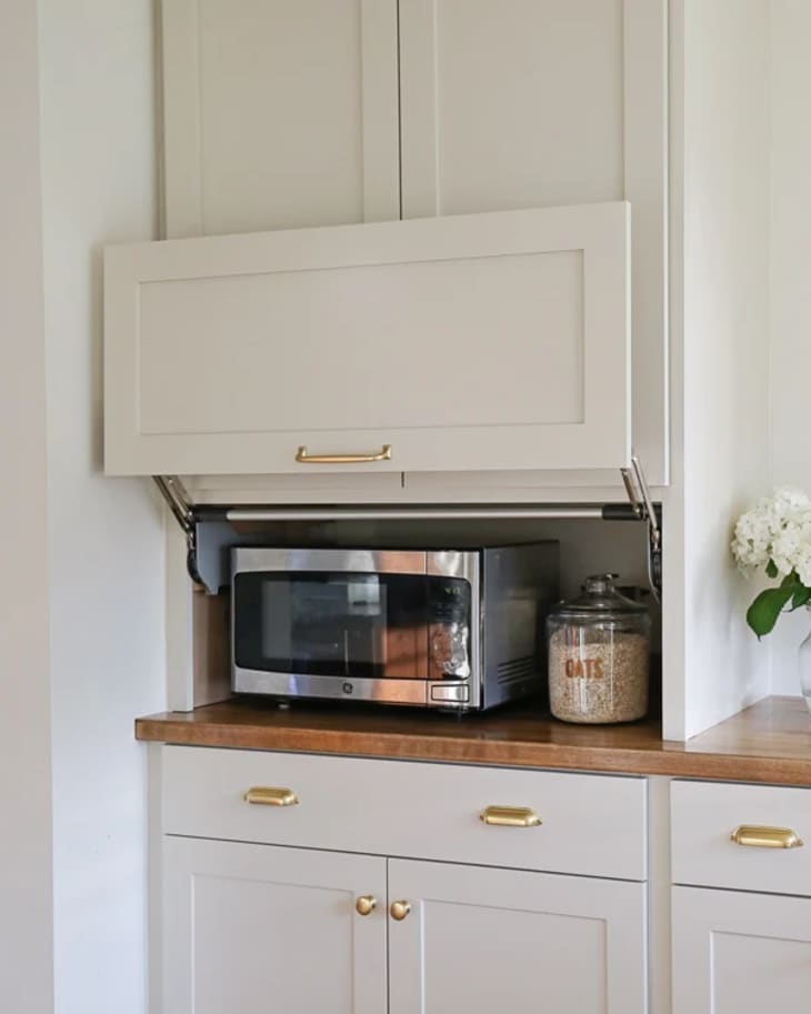 A kitchen's appliance garage features a levered door that reveals a microwave hidden behind it.