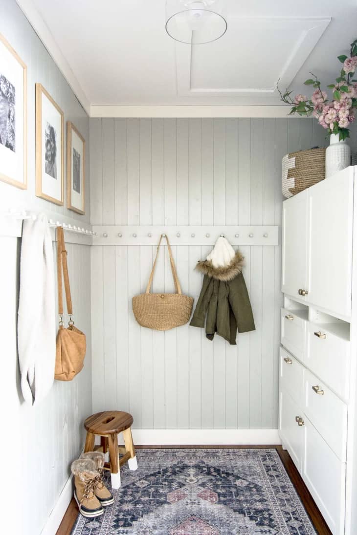 A peg rail mounted about halfway up the wall in a mudroom area holds coats and bags from its pegs.