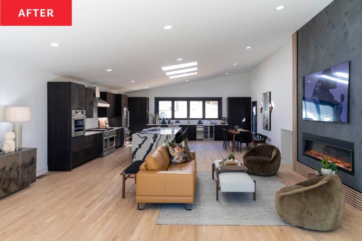 After: Open living room/kitchen area with a large gray cement-look fireplace, dark wood cabinets, and a light wood floor.