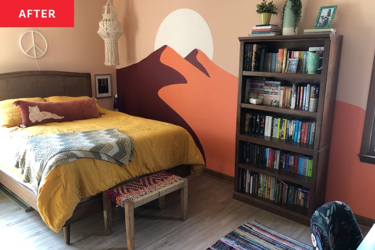 Bedroom after redecorating/mural painting. Mural wall has sunset/peach tones with 2 mountains and a sun. Bed has ochre/yellow linens, a tiger throw pillow, crocheted throw.There is a wood bookcase with books and a peace sign over the bed. Hanging macrame in corner