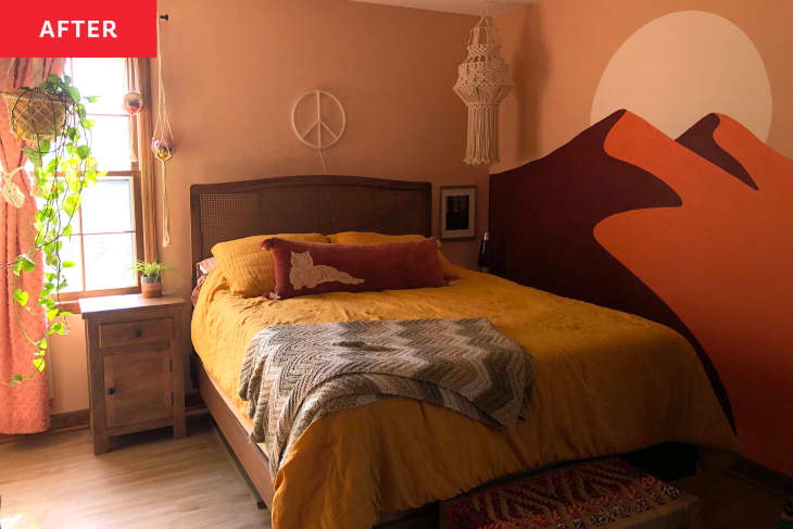 Bedroom after redecorating/mural painting. Mural wall has sunset/peach tones with 2 mountains and a sun. Bed has ochre/yellow linens, a tiger throw pillow, crocheted throw.There is a wood bookcase with books and a peace sign over the bed. Hanging macrame in corner