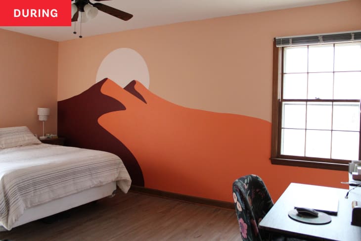 Bedroom after new wall mural has been finished, but before room has been redecorated. Mural is in peach and warm tones, and is a graphic painting of 2 mountain peaks with a sun.
