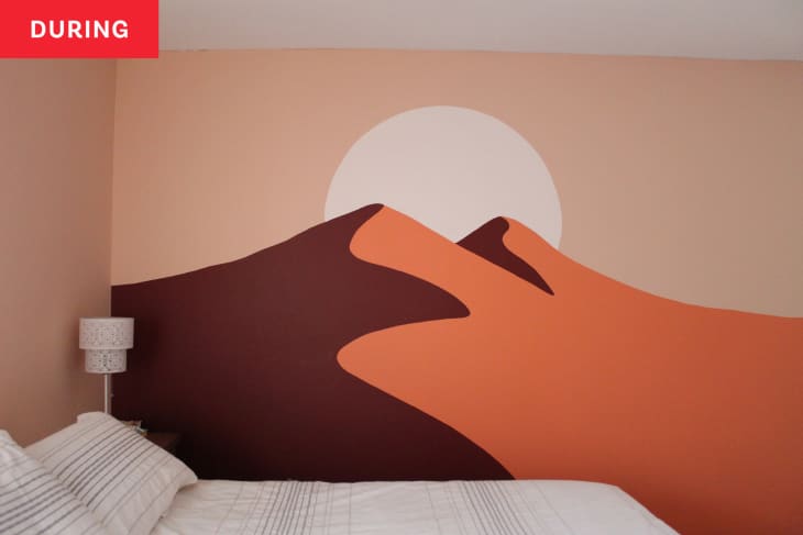 Bedroom after new wall mural has been finished, but before room has been redecorated. Mural is in peach and warm tones, and is a graphic painting of 2 mountain peaks with a sun.