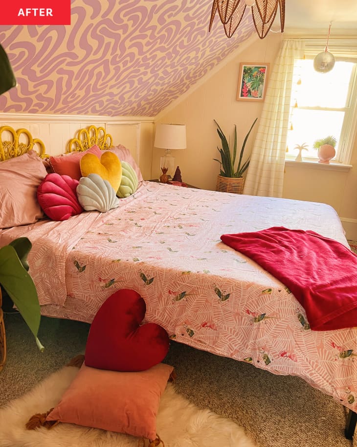 Bedroom after makeover. Painted lavender squiggly designs on angled ceiling, cane decorative headboard and bedside table, parrot-patterned bedspread, snake plant, velvet scallop shell and heart pillows, white shag rug with more velvet pillows