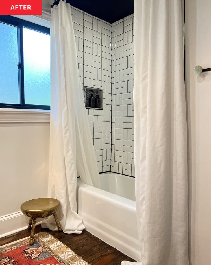 Bathroom after renovation: white walls, white tile with black grout over sink, vintage wood credenza as sink cabinet/bathroom counter, round mirror, gold hanging light fixtures, wood floor