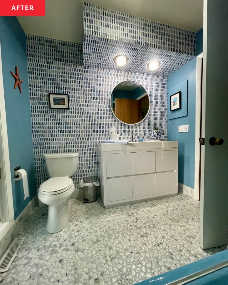 Bathroom after renovation. Blue walls, blue and white wallpaper accent wall over white vanity/sink, glass pebble flooring
