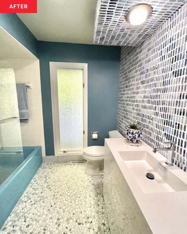 Bathroom after renovation. Blue walls, blue and white wallpaper accent wall over white vanity/sink, glass pebble flooring