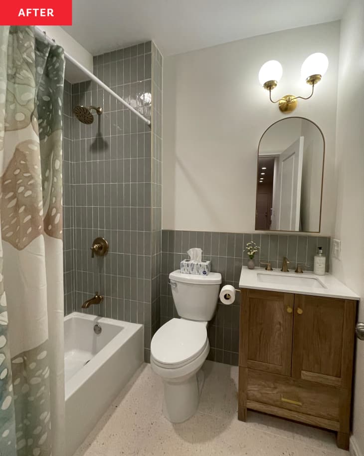 Bathroom after renovation with wooden vanity and tiled bath tub and wainscoting.