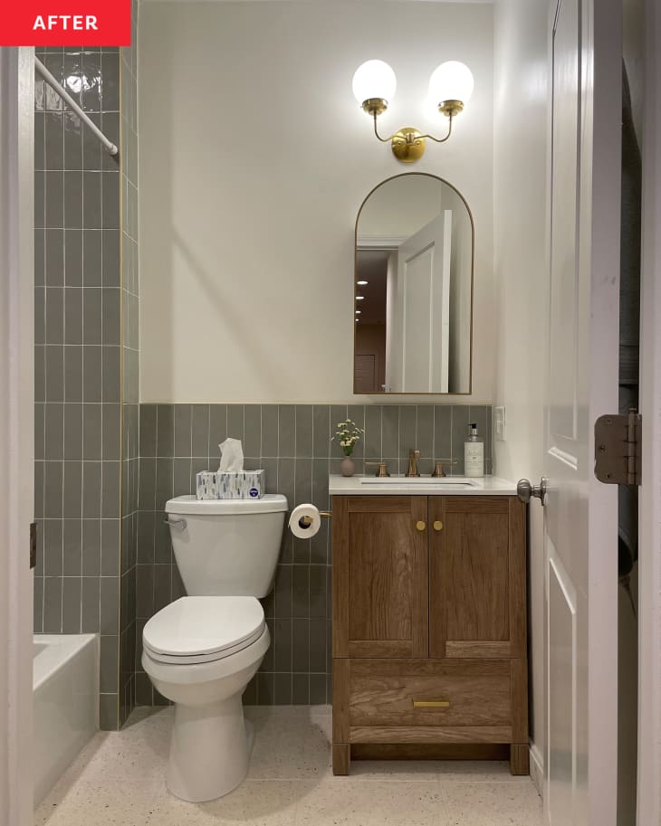 Renovated bathroom with grey tiles, wooden vanity and arched mirror after renovation.