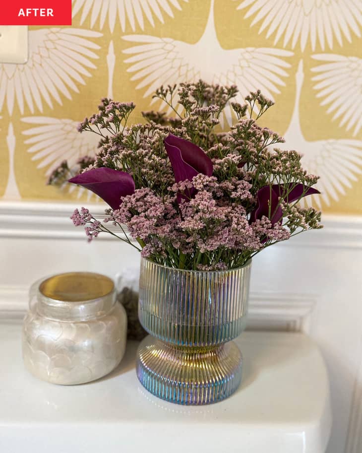 flowers and candle on toilet tank, white and gold patterned wallpaper behind