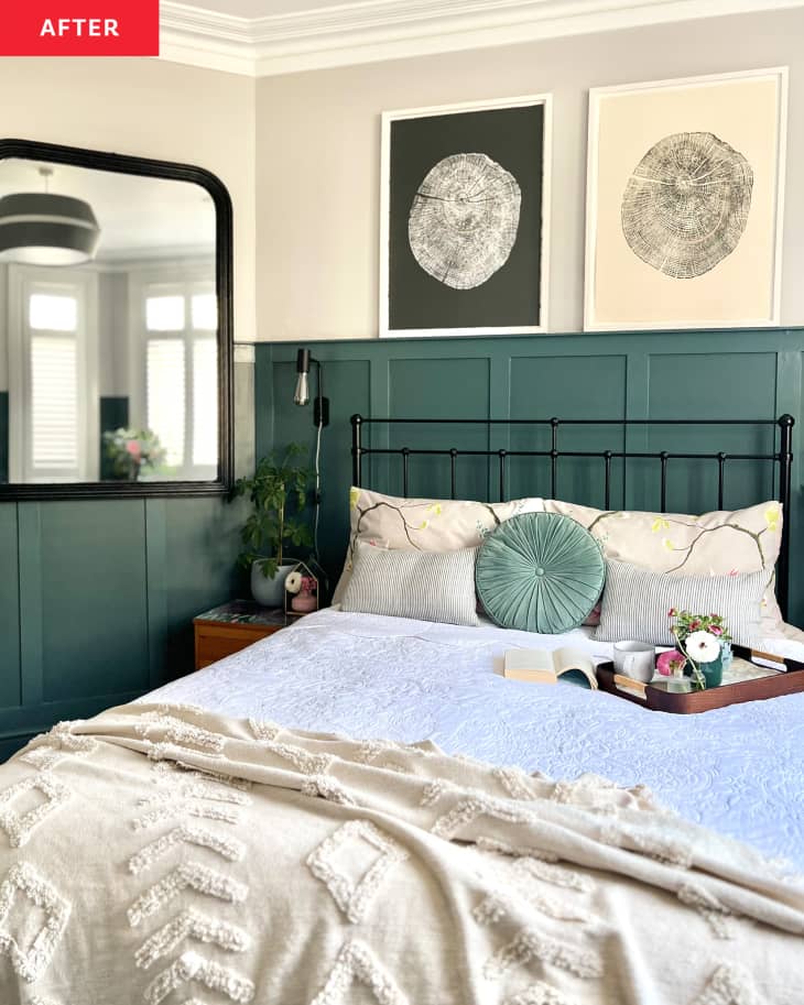 Bedroom after makeover. Wainscotting painted in a dark teal, bed with black metal bed frame, white, off white bedding with blue/green throw pillow, Large black-framed mirror on wall